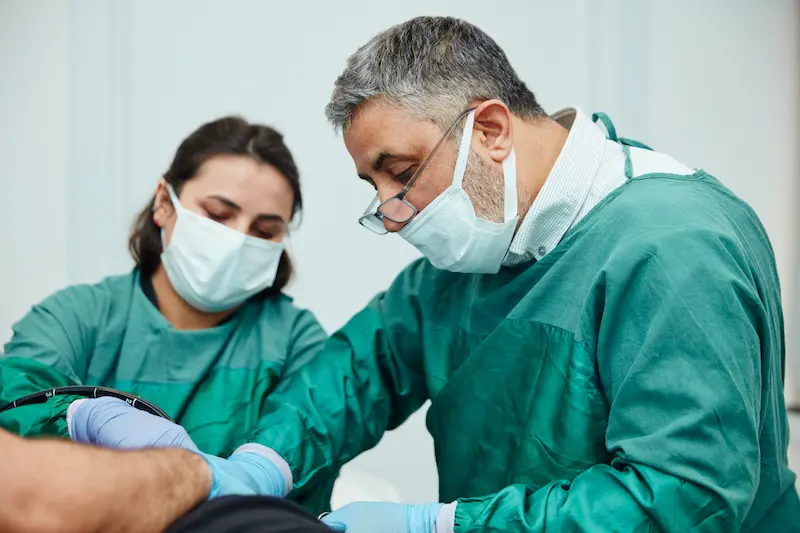 Proktoloji uzmanı Op. Dr. Selahattin Yitgin, klinik ortamında asistanı eşliğinde bir hastaya anoskopi cihazı ile detaylı hemoroid ve makat bölgesi muayenesi yapıyor.